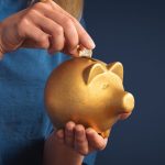 A woman putting a coin into a piggy bank.